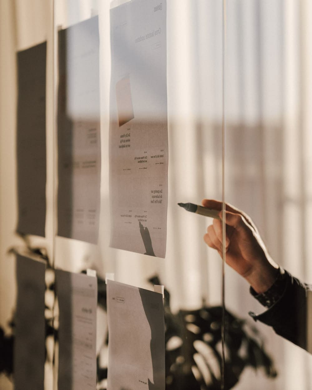 A hand pointing at project plans pinned to a glass wall in warm morning light